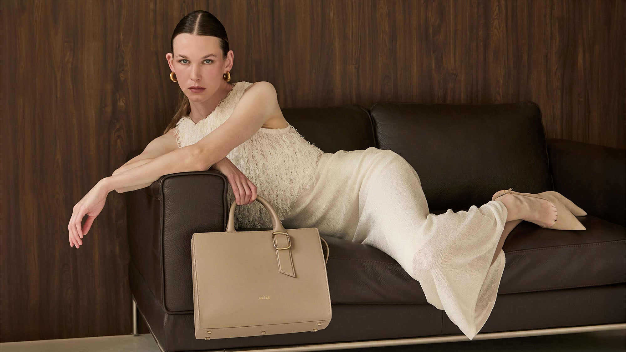Frau in cremefarbenem Kleid auf einer Ledercouch, daneben die Inea Midi in Sand Beige